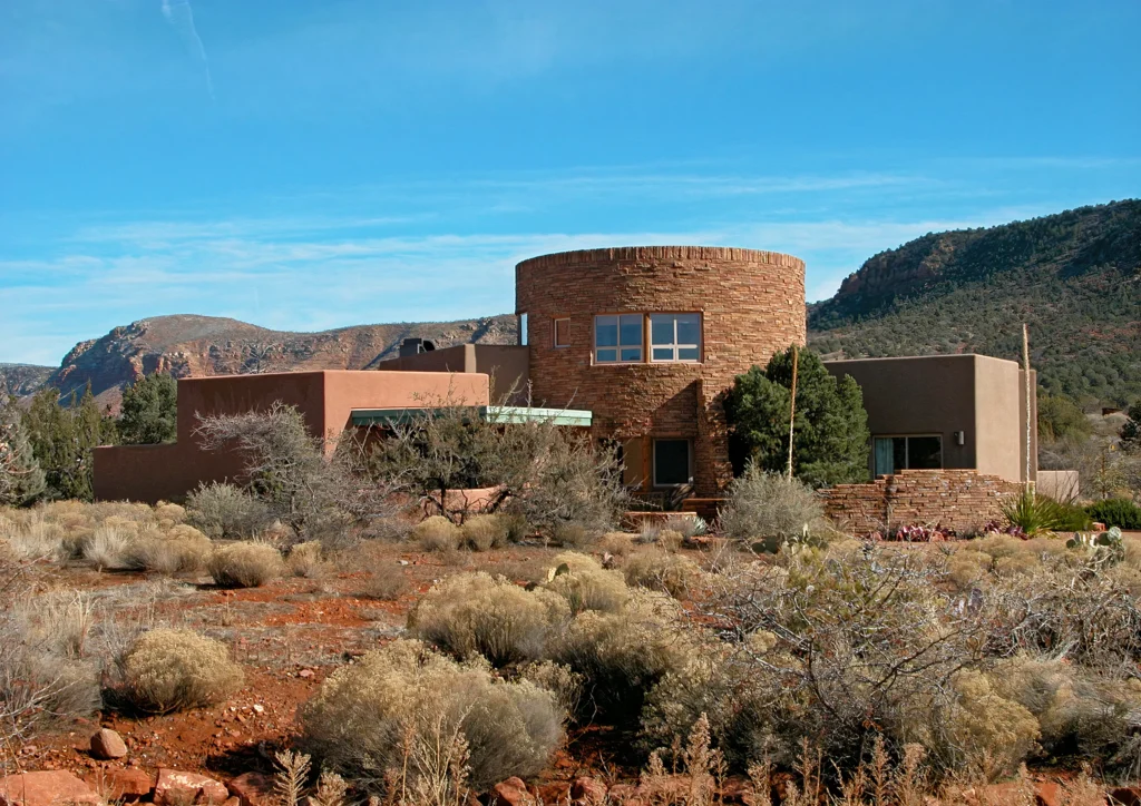 Sedona desert home with circular stone tower framed by red rock cliffs and natural landscaping.