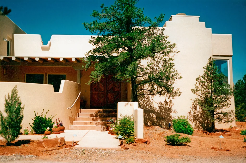 Entry facade of a Sedona home designed by architect Paul Cate, with Pueblo-style stucco walls, wood front doors, and desert landscaping.