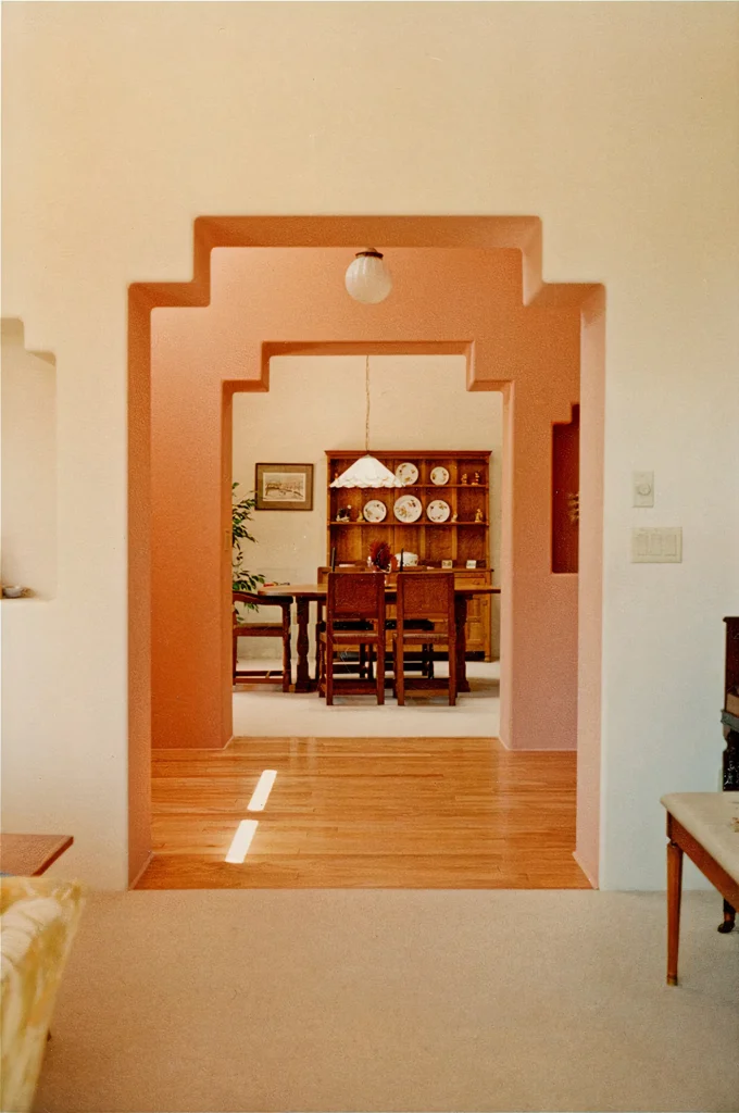Southwestern interior with a stepped plaster archway framing a dining room with wood table and hutch.