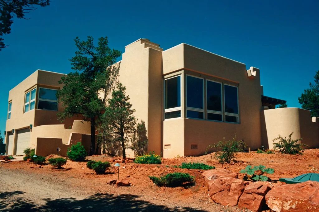 Southwestern-style residence with clean stucco forms and large corner windows above red rock landscaping.