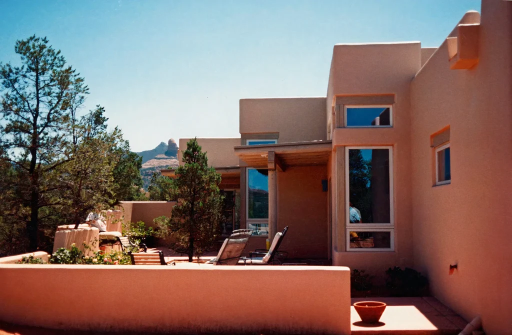 Stucco terrace at this fine home with lounge chairs, trees, and a distant red rock spire.