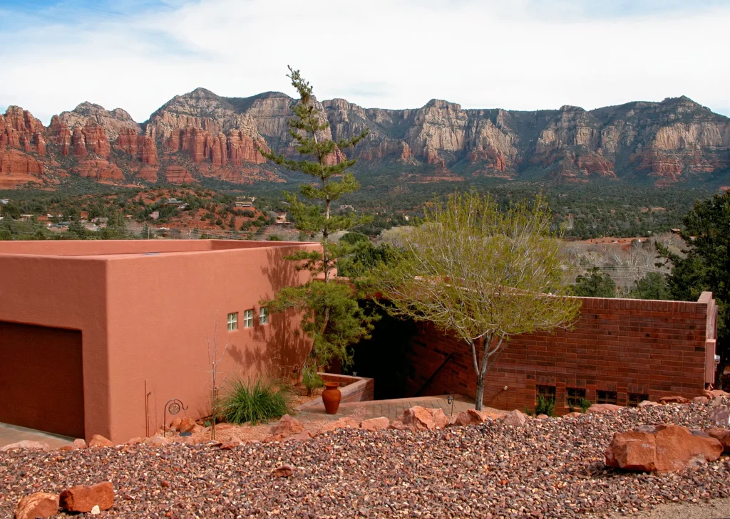 Contemporary red stucco home designed by architect Paul Cate, set low against a wide panorama of Sedona red rock cliffs and forested foothills.