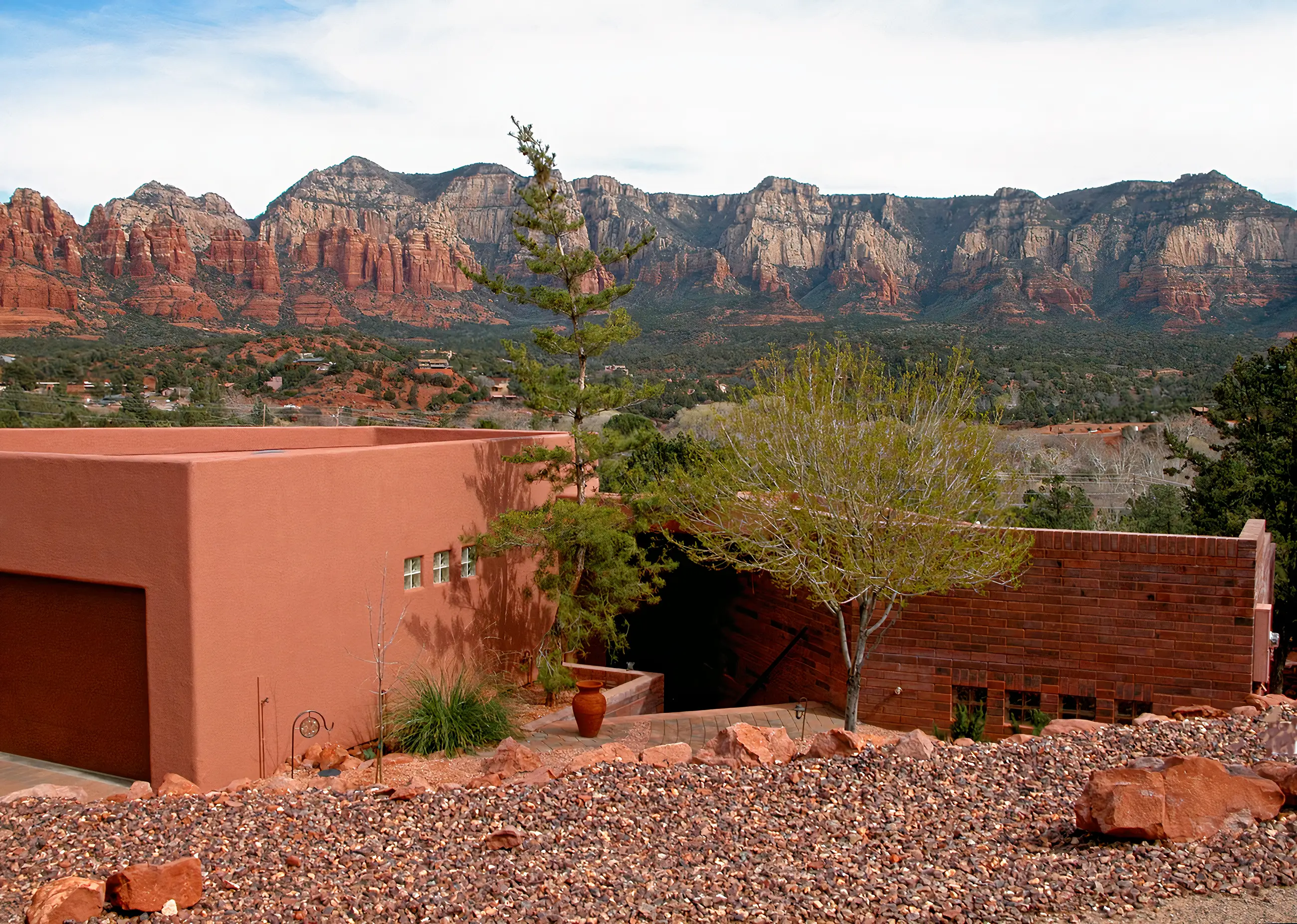 Contemporary red stucco home designed by architect Paul Cate, set low against a wide panorama of Sedona red rock cliffs and forested foothills.