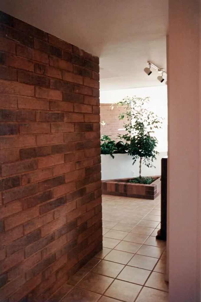 Interior hallway with warm brick wall, tiled floor, and built-in planter holding a small indoor tree and lush greenery.