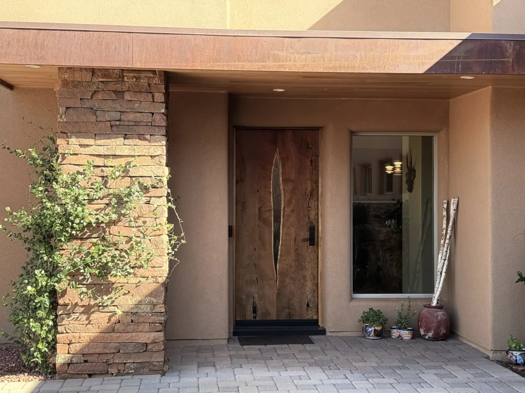 Front entry with a sculpted wood door and stacked-stone column against a stucco façade.