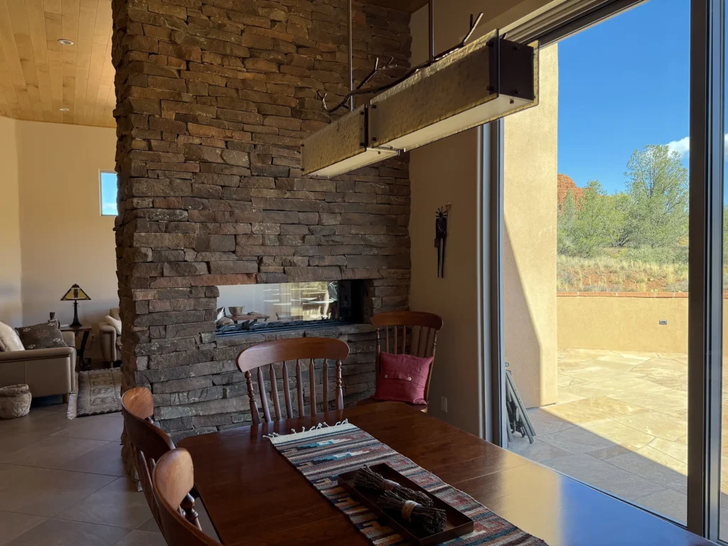 Dining area beside a stone fireplace wall with large windows opening to the Sedona landscape.
