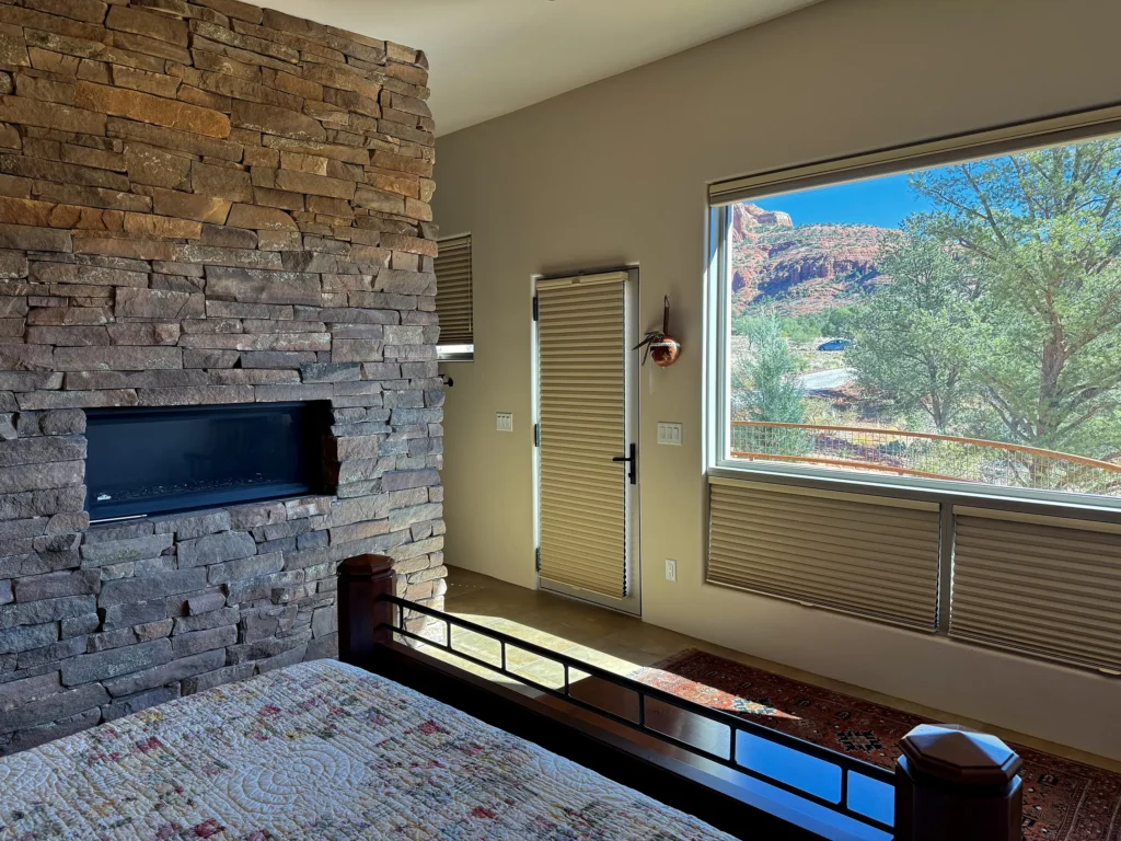 Bedroom with stone fireplace wall and large window overlooking a beautiful red rock landscape.