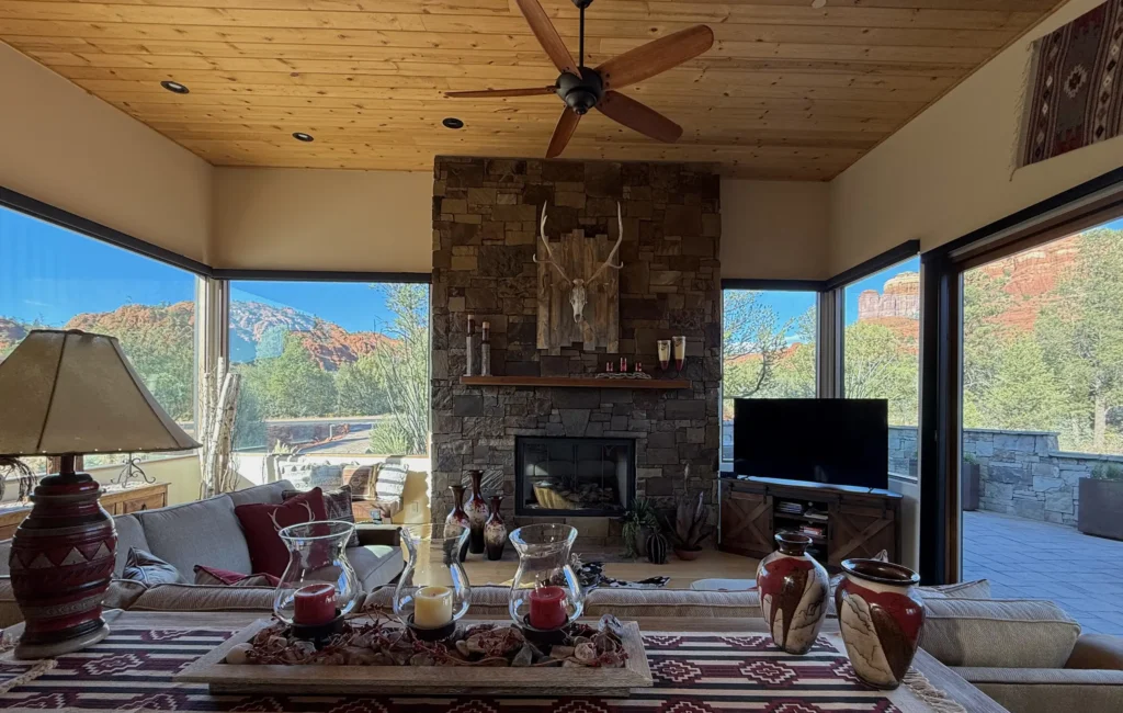 Living room with stone fireplace wall and large corner windows framing Sedona’s red rock landscape.