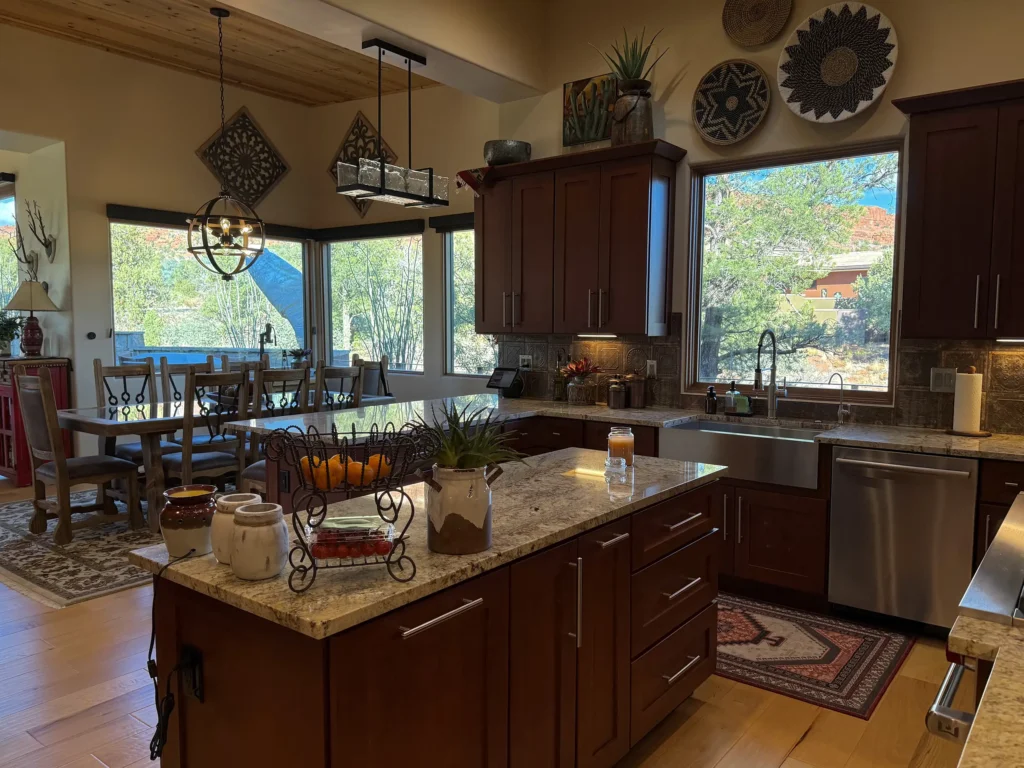 Kitchen and dining area with warm wood cabinetry and big windows looking out to trees and red rocks.