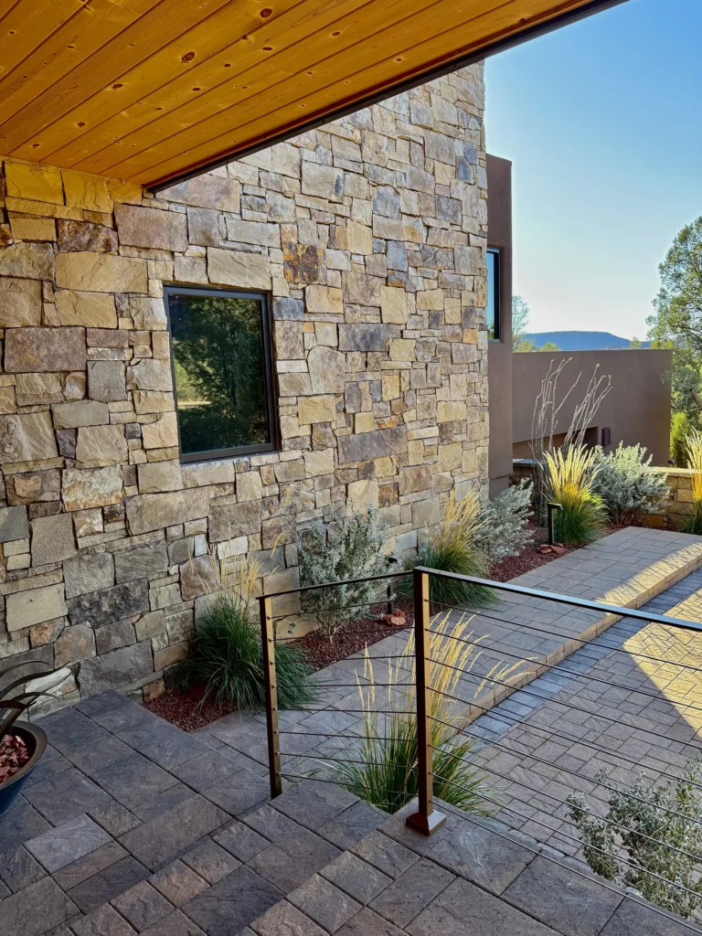 Stone-clad exterior wall and entry steps bordered by desert planting.