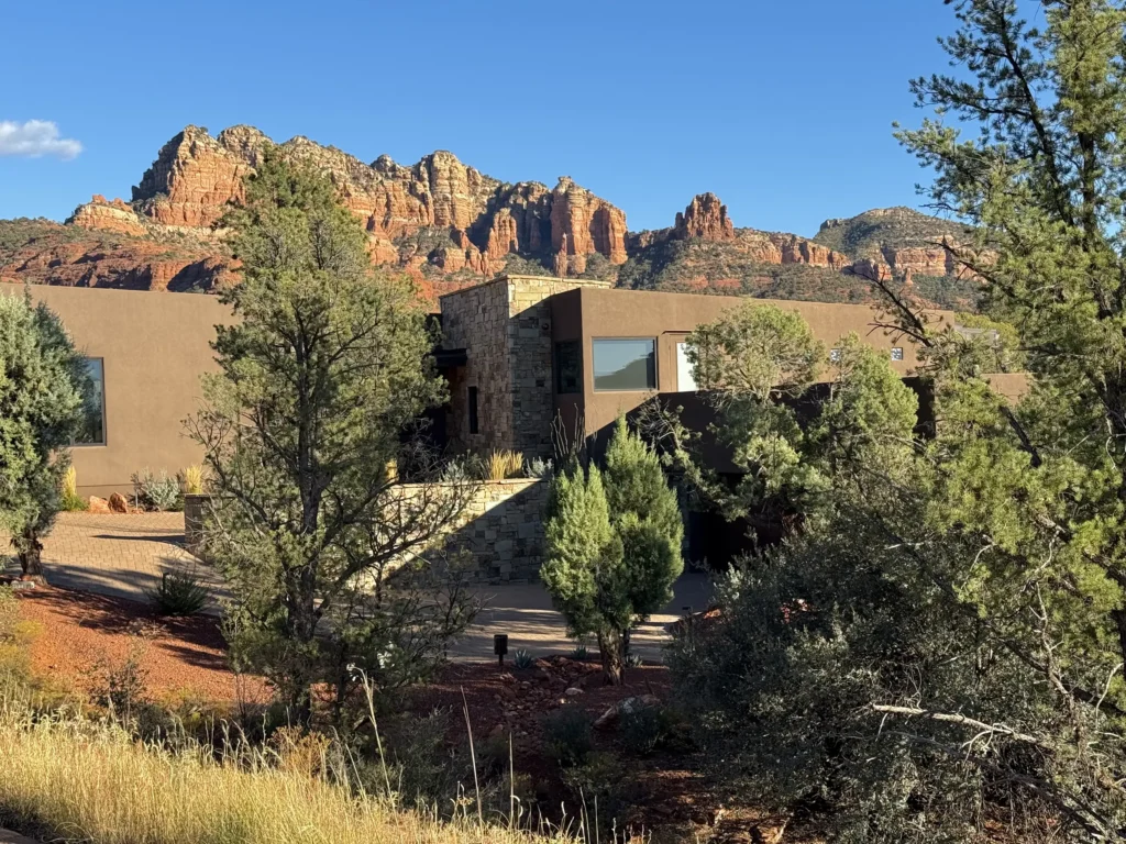 Sedona residence designed by architect Paul Cate nestled among trees with dramatic red rock cliffs rising behind the home.
