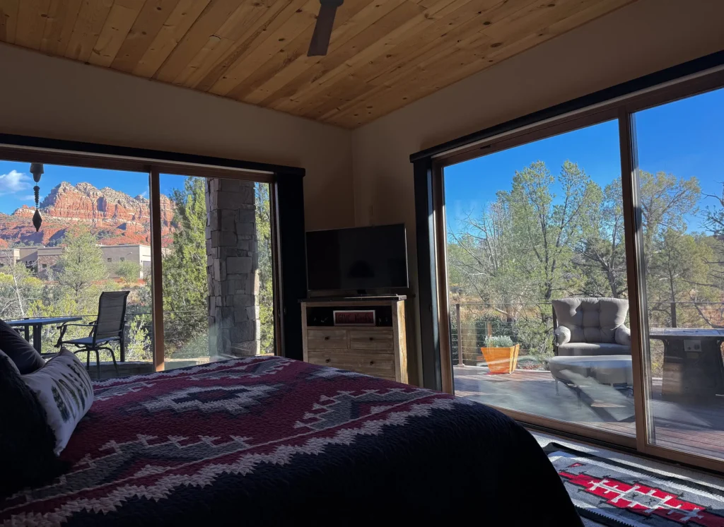 Bedroom with wood ceiling and sliding glass doors on two sides overlooking a deck and red rocks.