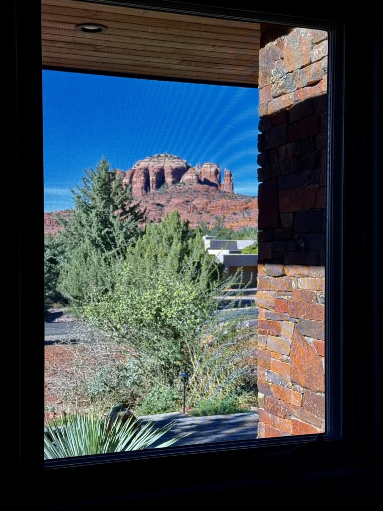 Framed view of Cathedral Rock and desert landscaping seen through a single window with stacked red-rock column.