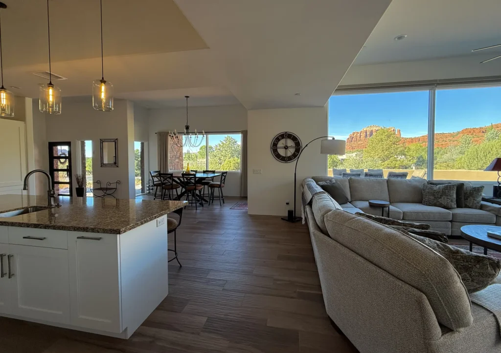 Open-concept kitchen, dining, and living area with large sectional sofa and picture windows framing Sedona red rock and treetop views.