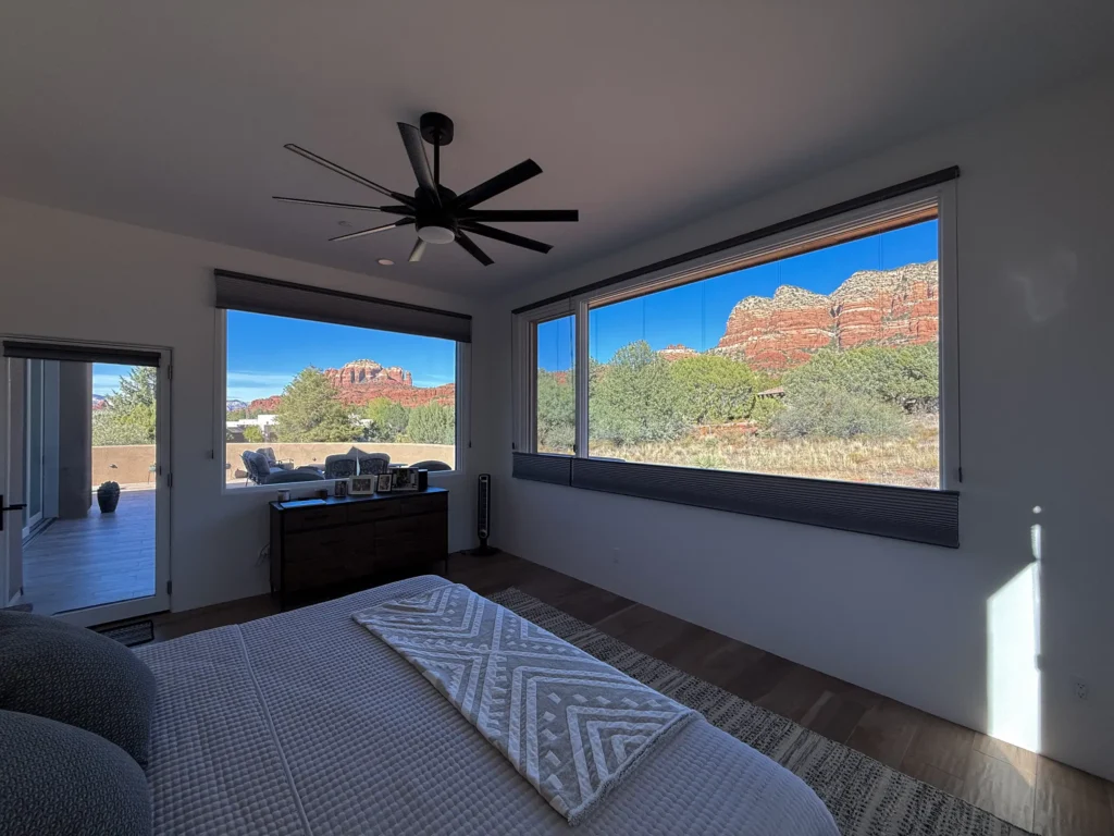 Bedroom with panoramic windows showcasing Sedona red rock formations and desert vegetation beyond a private patio.