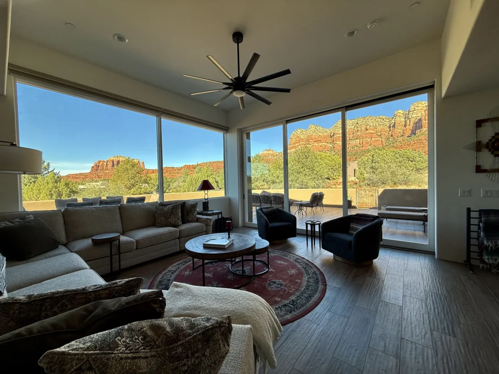 Living room with sectional sofa and wide glass walls opening to a terrace and expansive red rock vistas.