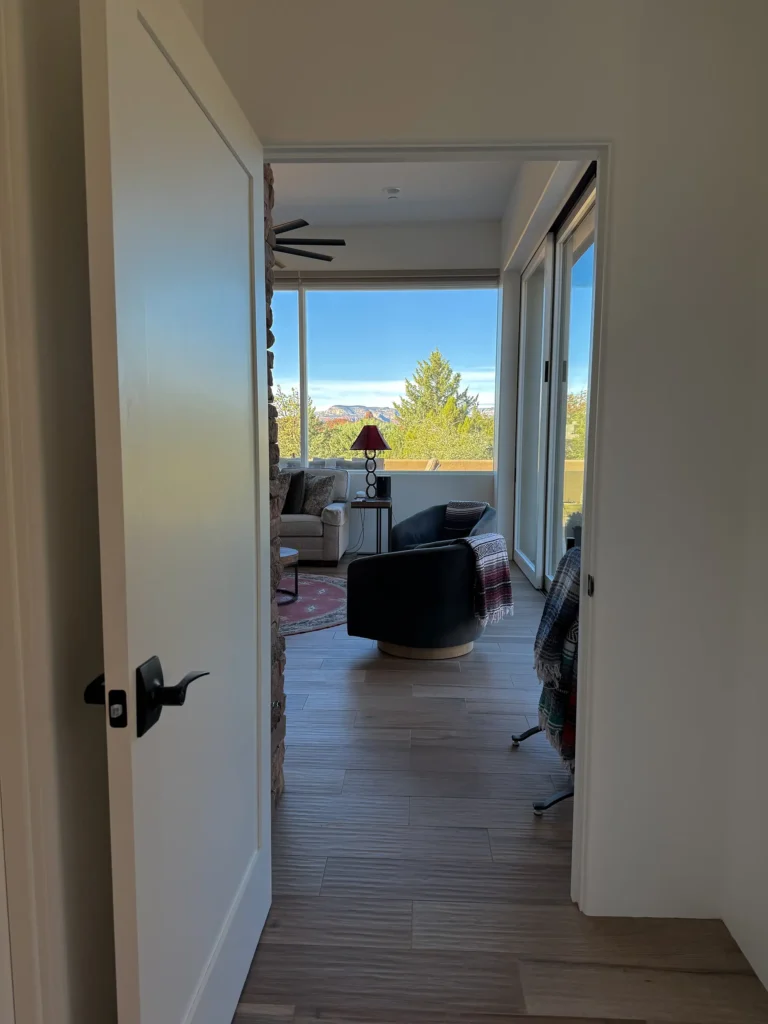 Hallway view toward the living room, highlighting wood-look flooring and a large window framing treetops and distant red rocks.