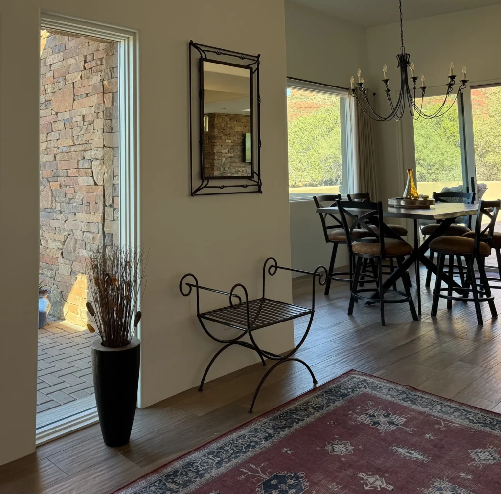 Dining nook with round table and chandelier, adjacent to a doorway revealing the home’s stacked-stone exterior wall and outdoor pavers.