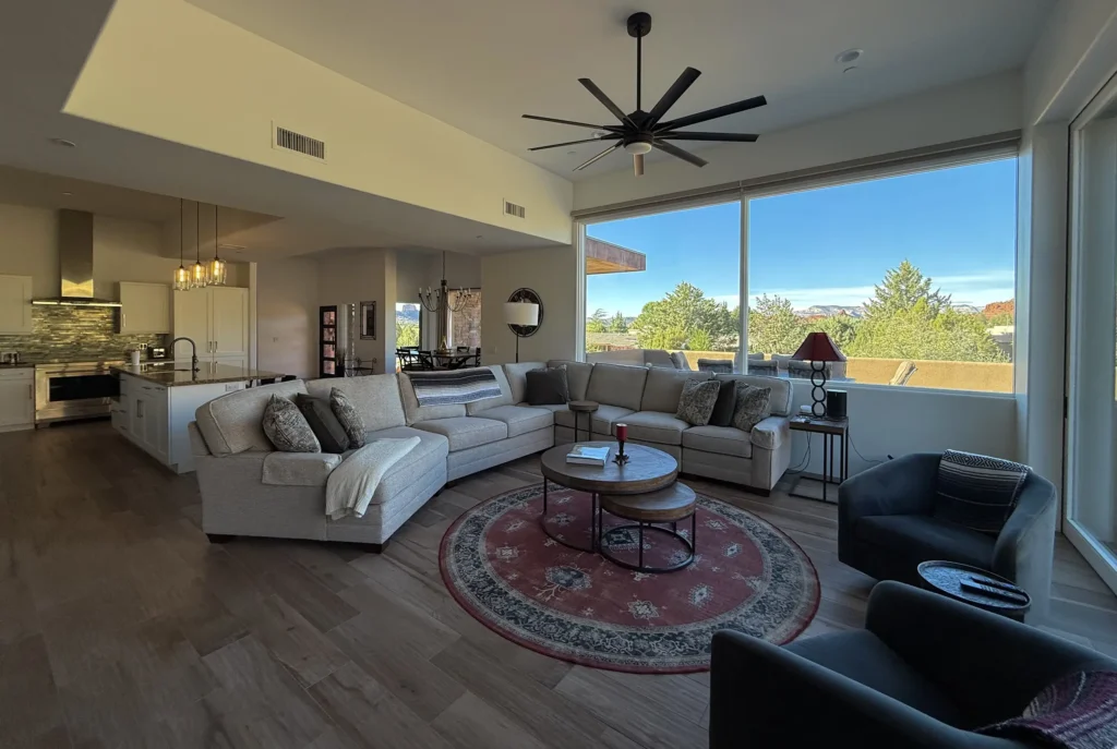 Open great room in a Paul Cate–designed Sedona home, with large sectional sofa, modern ceiling fan, and floor-to-ceiling windows looking out to red rock and treetop views.