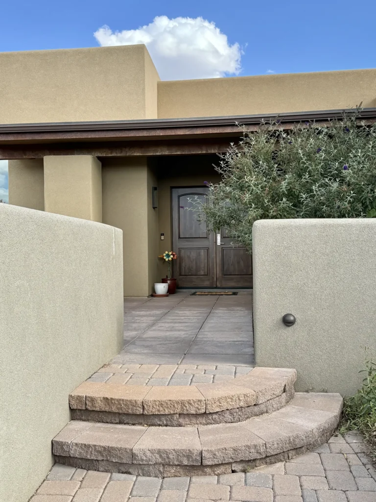 Front entry steps and porch of a Southwestern stucco home with wood double doors and lush desert plantings.